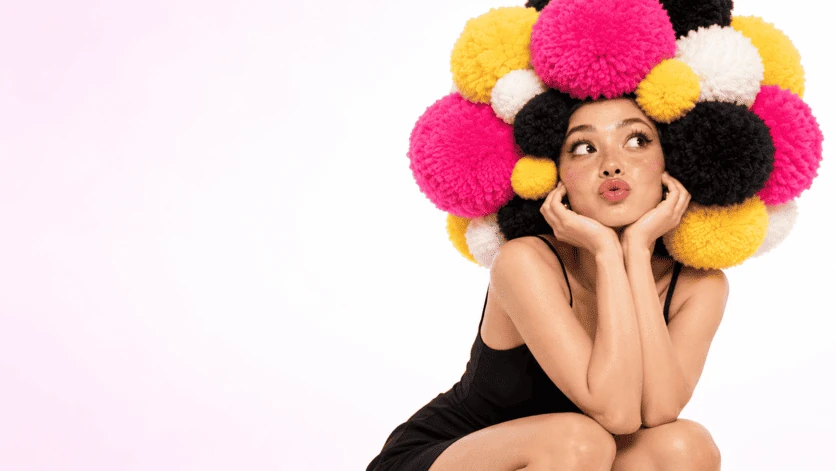 Character with pink, yellow and black pompom hairstyle on light background